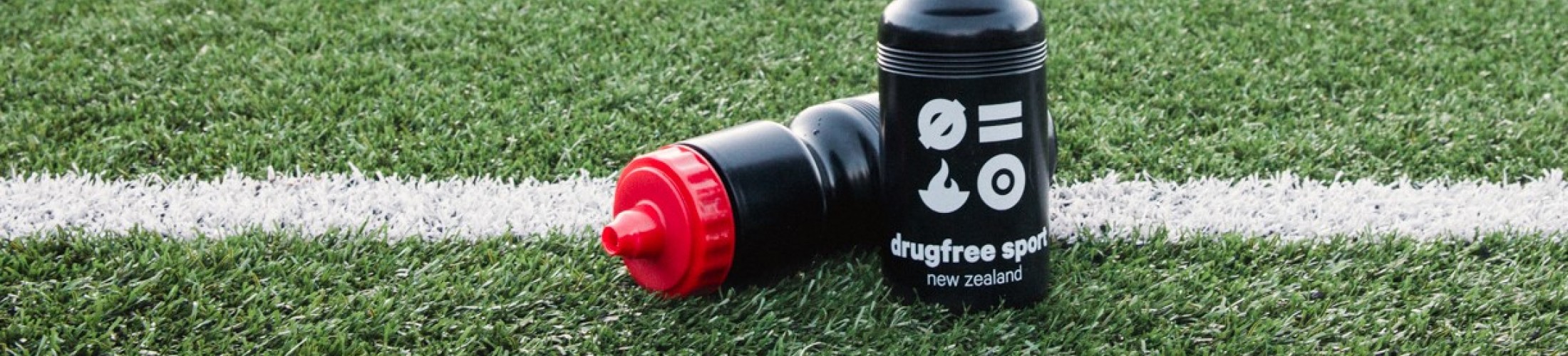 DFSNZ drink bottles on the side of a football pitch.